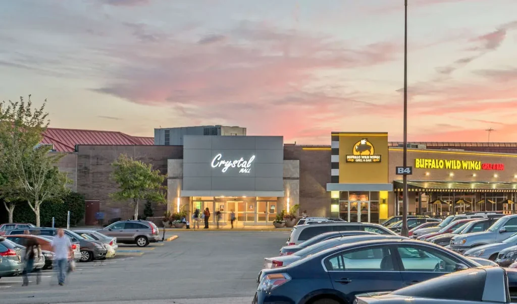 A bustling mall entrance with a grand brick building and parked cars, creating a vibrant ambiance of shopping and excitement.