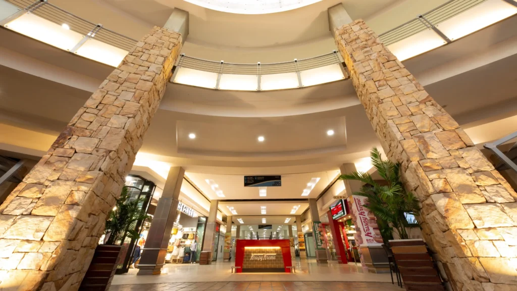 Inside Clearwater Mall: Shoppers browsing stores, escalators leading to different levels, vibrant displays, and bustling activity.