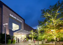 Entrance to Fairlane Town Center mall at night, illuminated by bright lights and surrounded by parked cars.