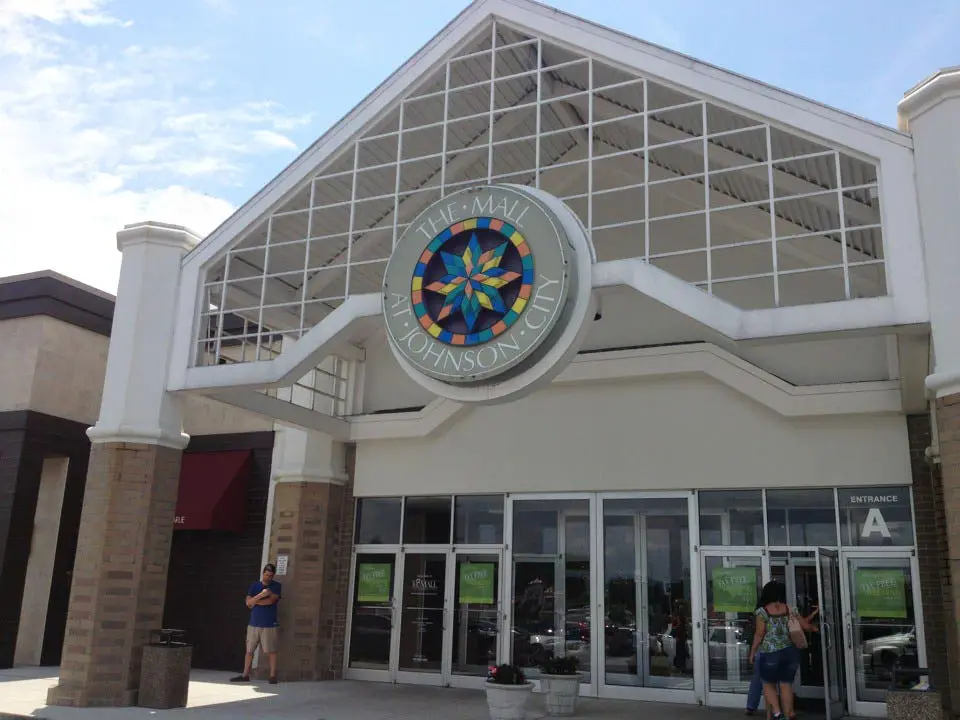 A vibrant mall entrance with glass doors, adorned with colorful banners and a welcoming atmosphere.