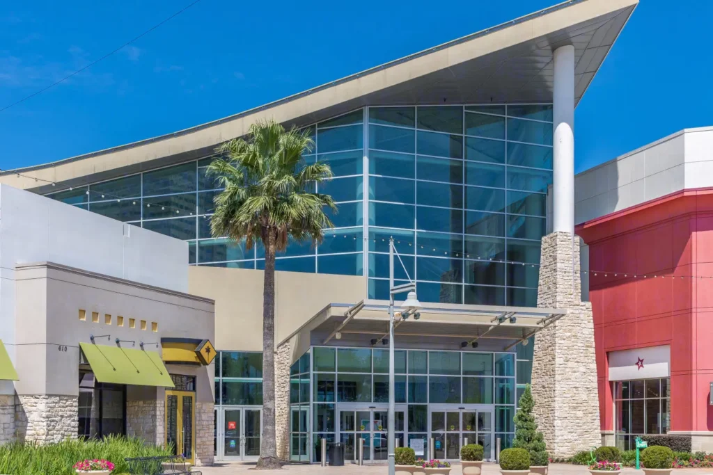 A shopping center, Memorial City Mall, featuring a spacious building surrounded by palm trees.