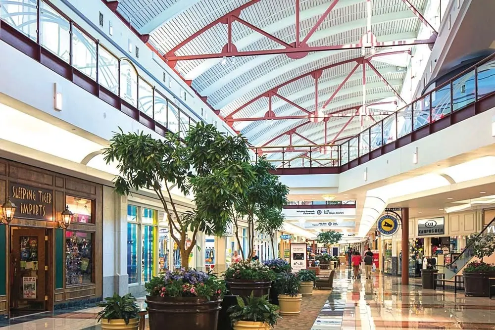 A bustling mall, RiverTown Crossings, adorned with numerous shops and lush green plants.