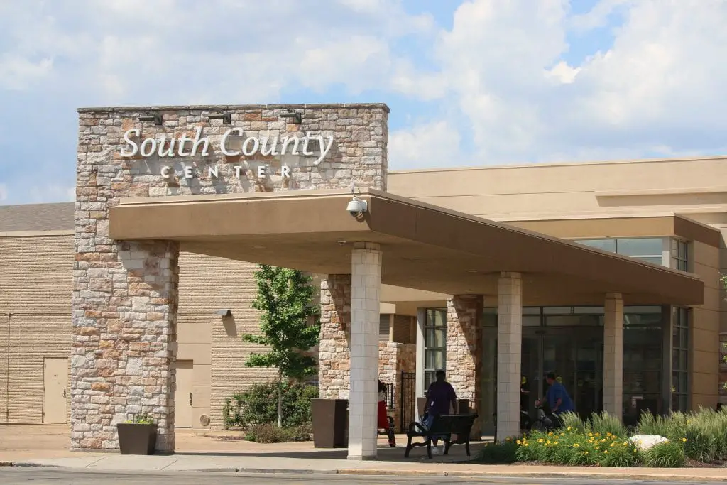 Shopping mall entrance with sign "South County Center" surrounded by palm trees and blue sky.