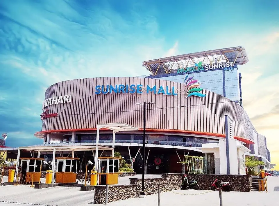 Exterior of Sunrise Mall with palm trees and colorful banners.