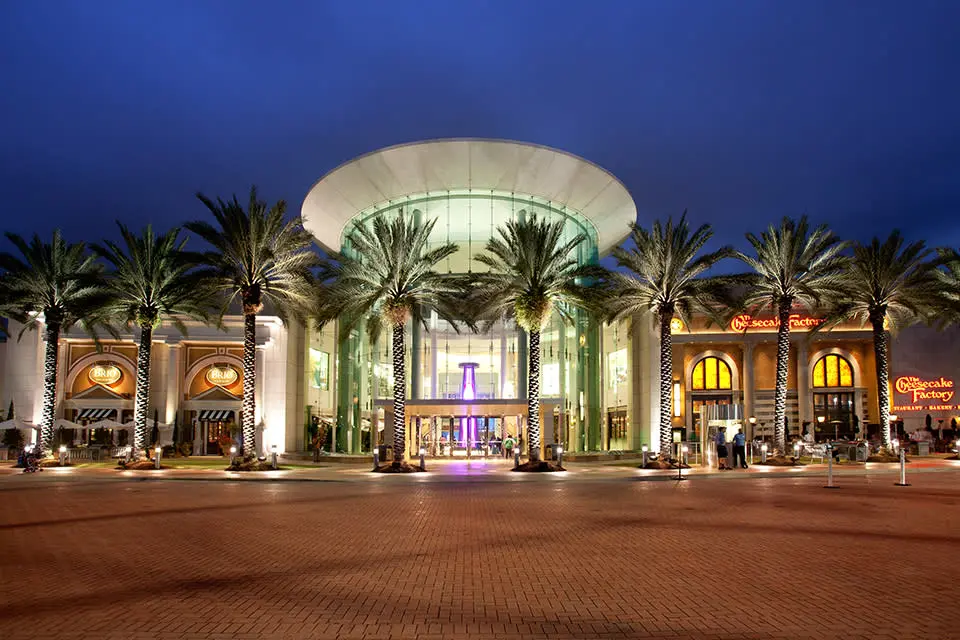 A large shopping center with palm trees and lights at The Mall at Millenia.