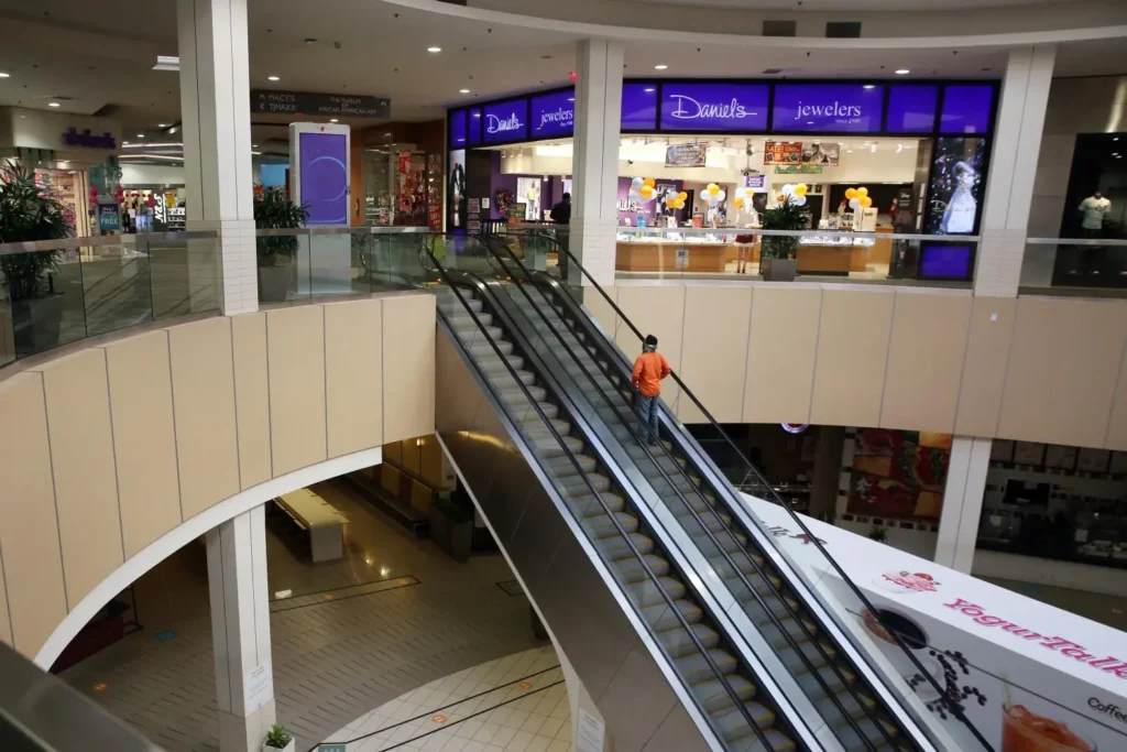 A modern mall with escalators and a towering building in the background.