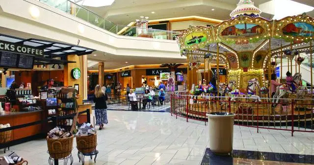 A carousel in the center of a bustling mall, brightly colored horses and chariots ready for riders.