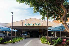 A bustling shopping mall with stores, escalators, and shoppers carrying bags.