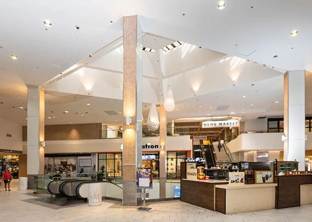 Spacious shopping mall interior with high ceiling, filled with stores and shoppers.