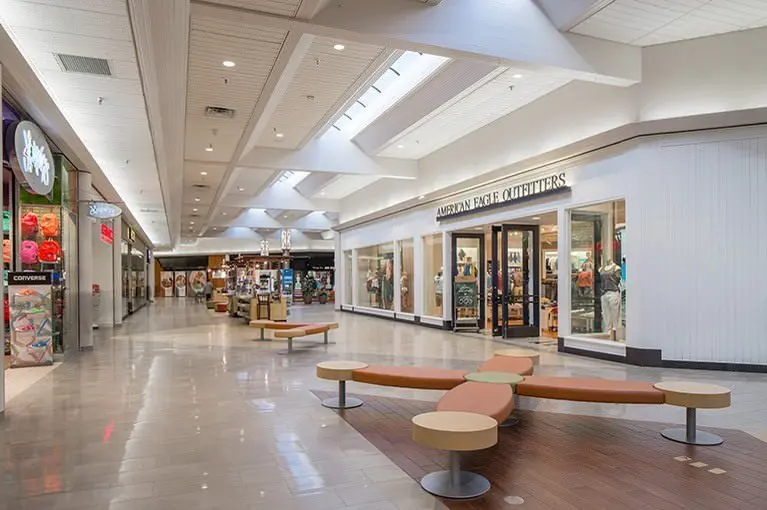 A bustling mall with numerous shops and benches, offering a variety of retail options and seating areas.