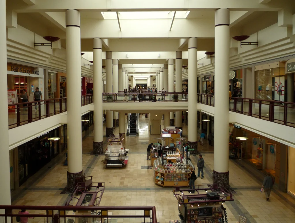 A crowded mall with shoppers walking around, browsing stores, and carrying shopping bags.