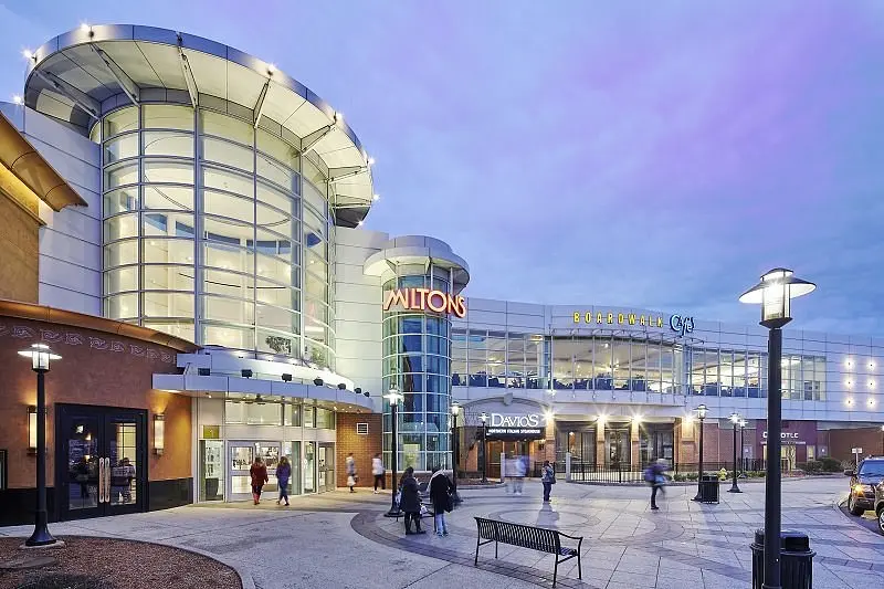 A bustling shopping center with shoppers walking around, carrying bags and browsing stores.