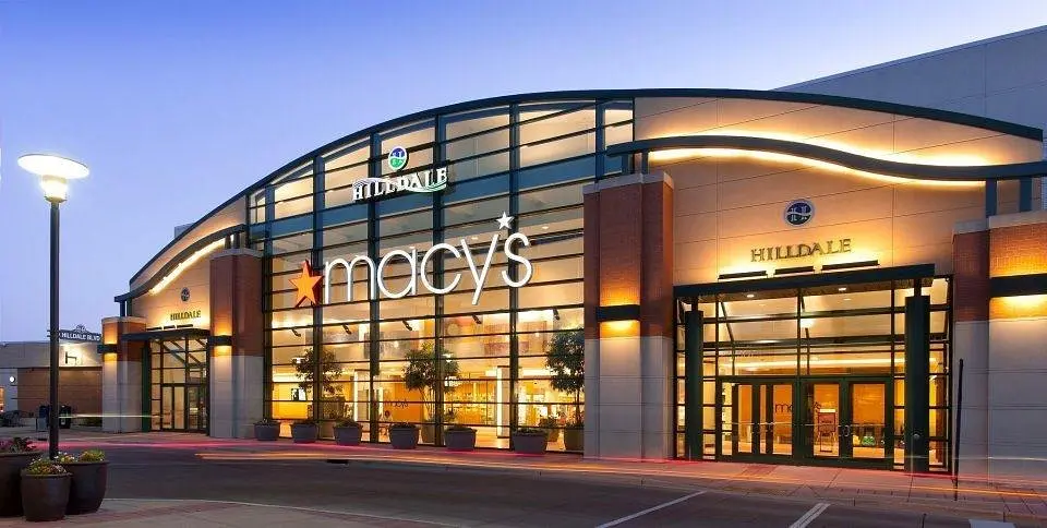 Macy's store in shopping center at dusk, with glowing lights and bustling shoppers.