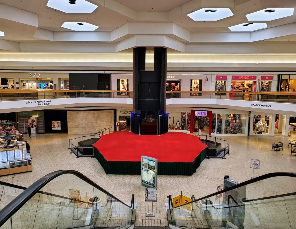 Red carpet in mall, leading to shops and surrounded by people shopping.