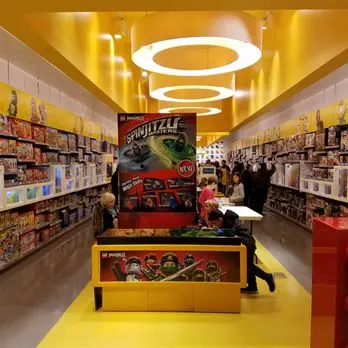 A Lego store with yellow floors and shelves, showcasing colorful building blocks and accessories.