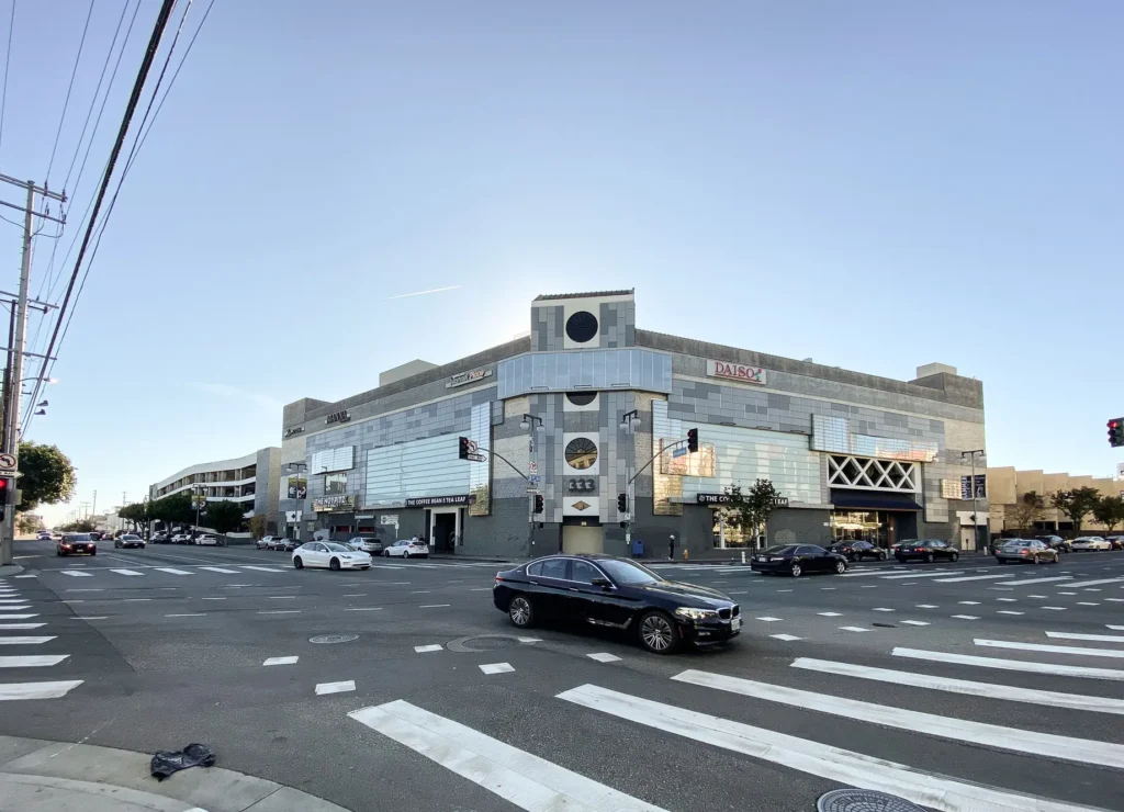 A car driving down a street in front of a building in Little Tokyo Galleria.